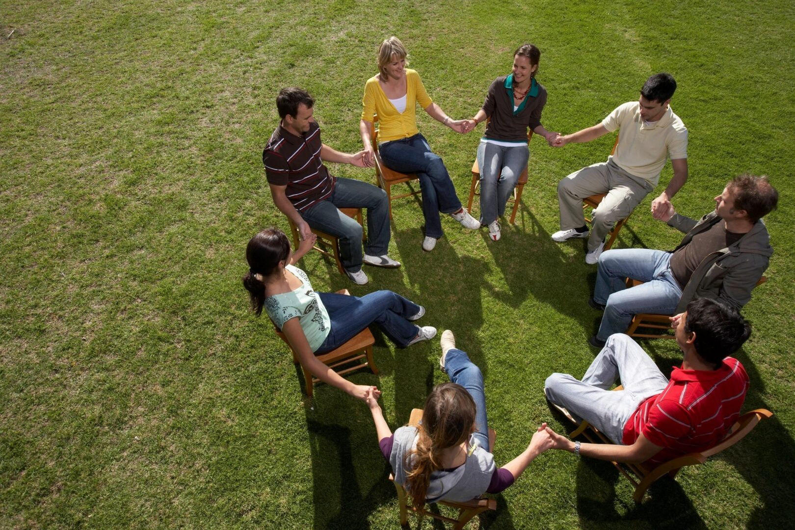 A group of people sitting in the grass holding hands.