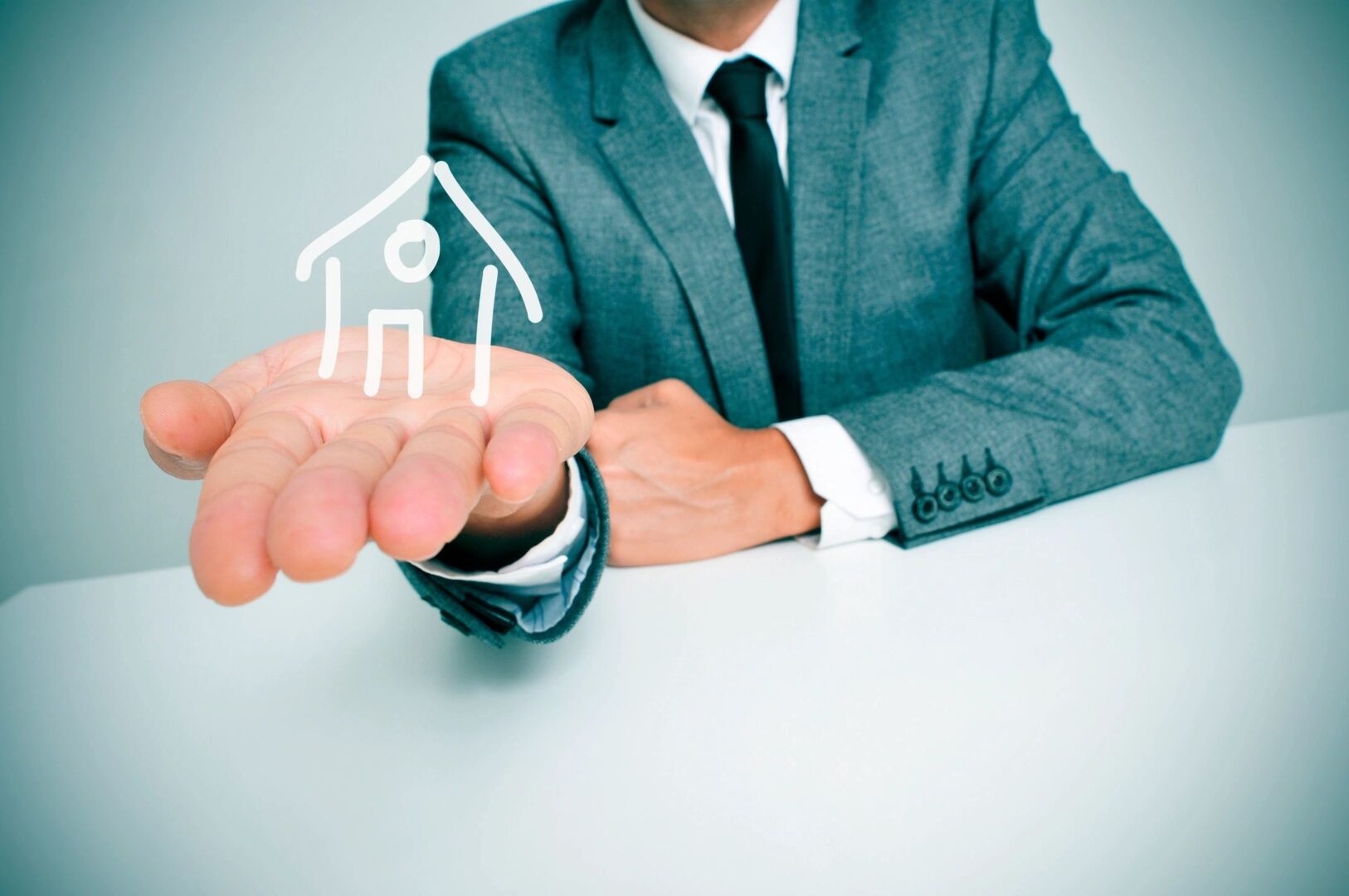 A man in a suit holding out a paper house.